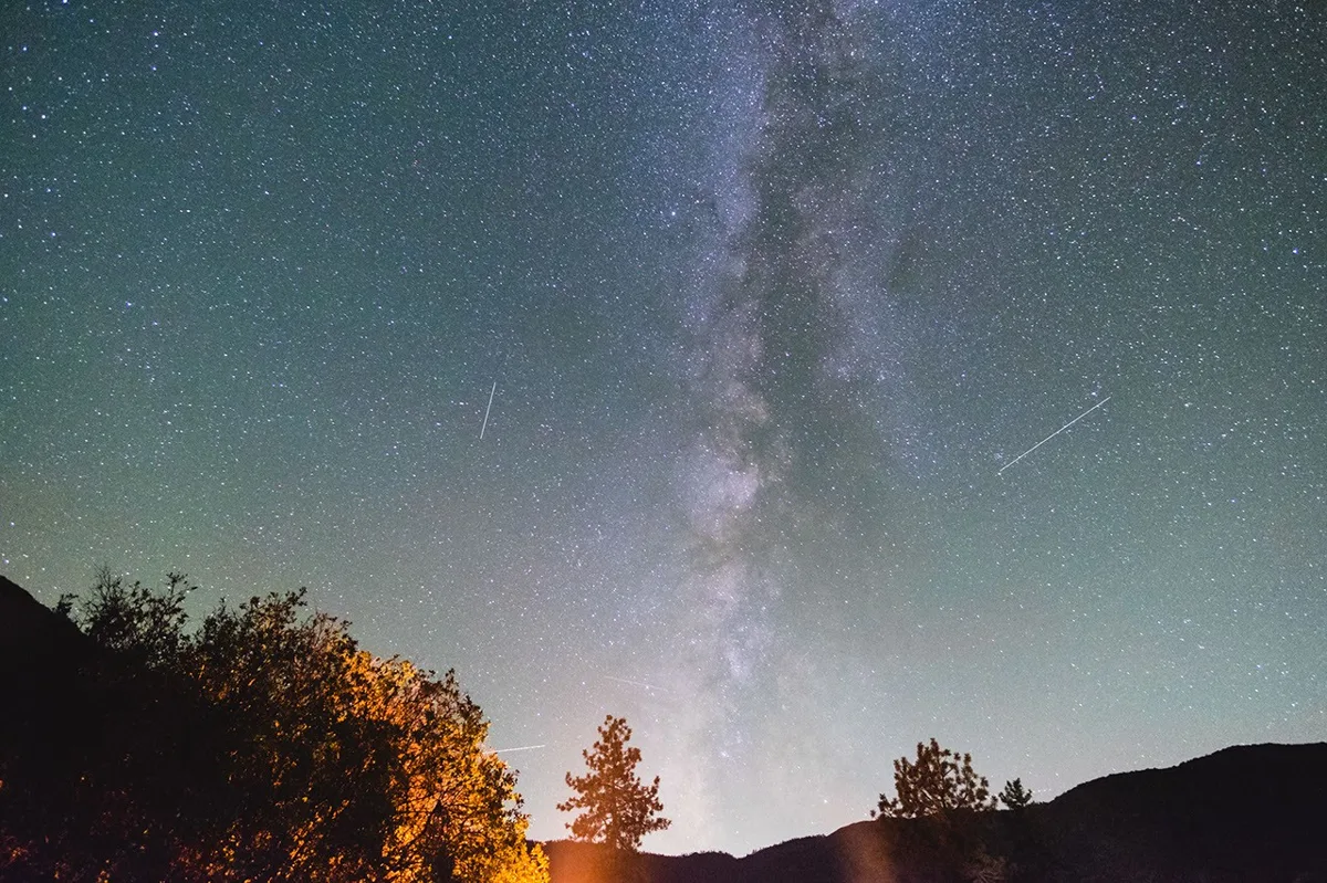 Imagem do céu noturno com Saturno, estrelas e meteoros