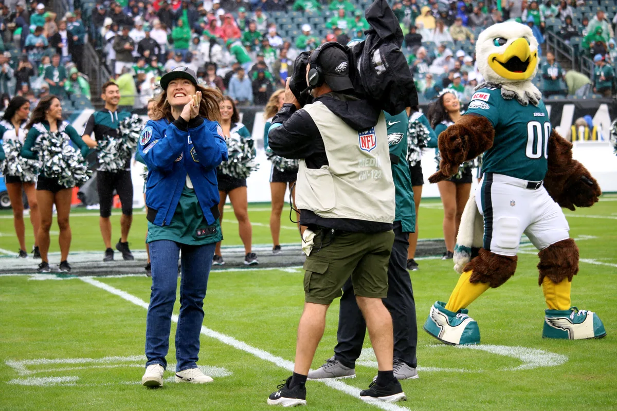Christina Koch cantando na arquibancada de estádio durante jogo da NFL