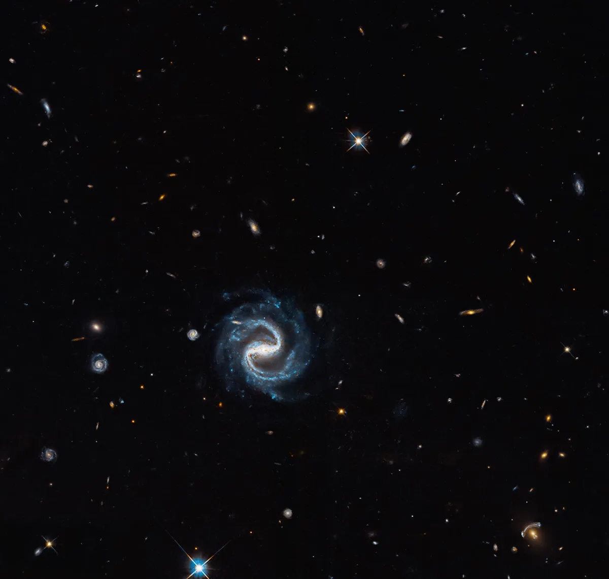 Imagem de uma galáxia em espiral com efeito de lente gravitacional ao redor, capturada pelo telescópio Hubble.